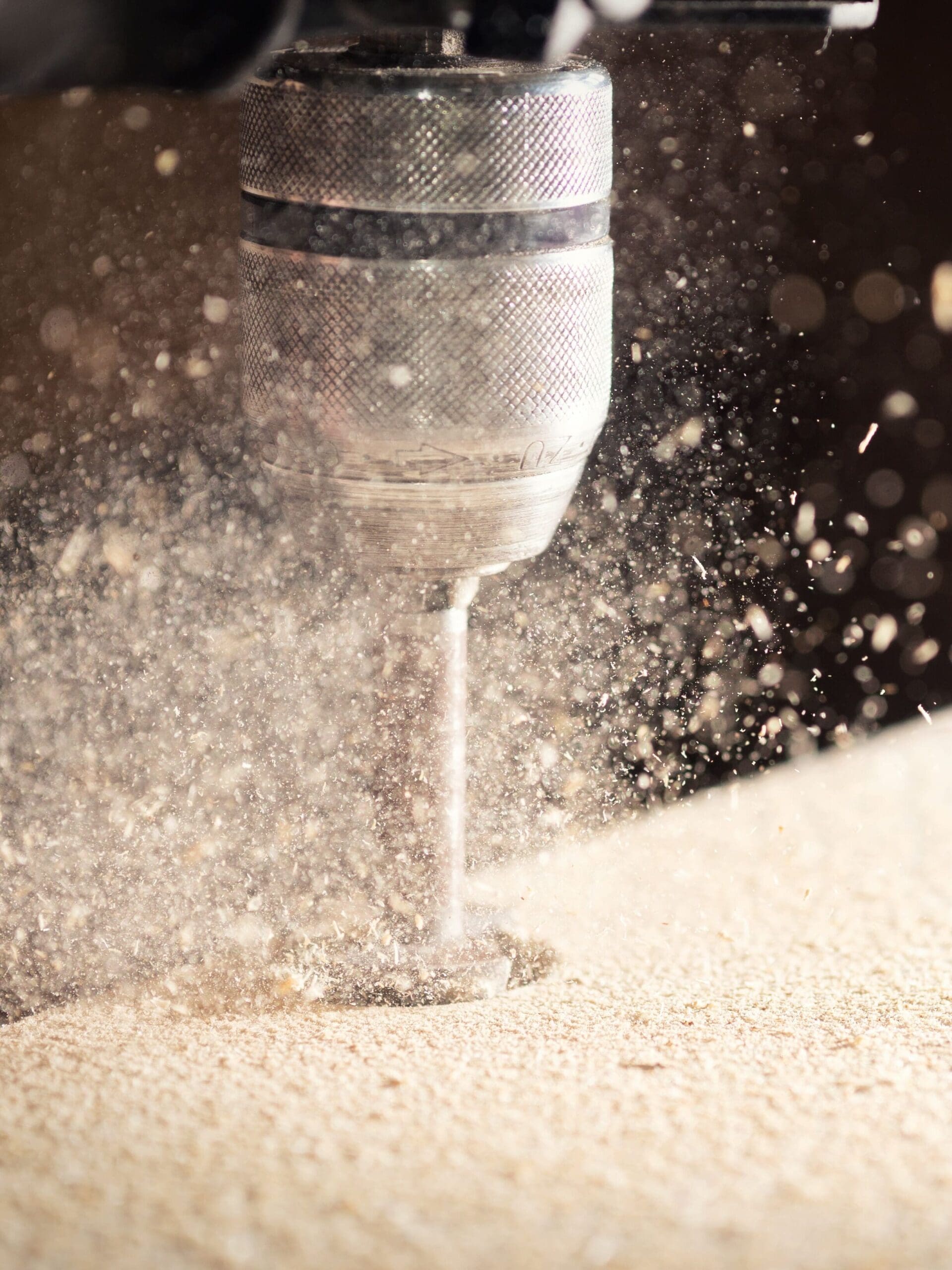 Dust flying while someone drills into a wooden board.